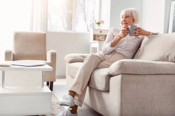 Petite äldre kvinna dricka kaffe i hennes vardagsrum — Stockfoto