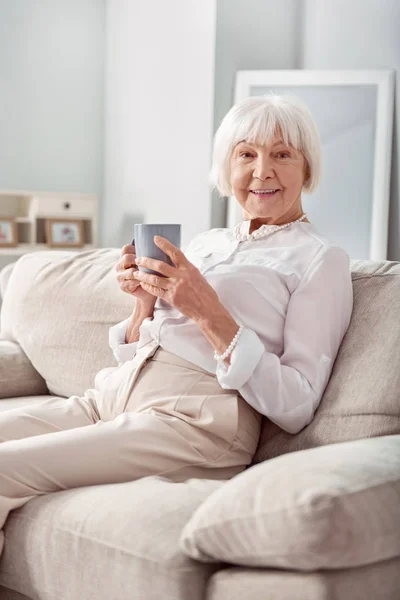 Bájos idősebb nő pózol a csésze tea a kanapén — Stock Fotó
