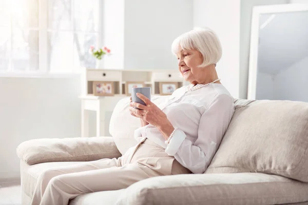 Příjemný starší žena pít čaj na gauči — Stock fotografie