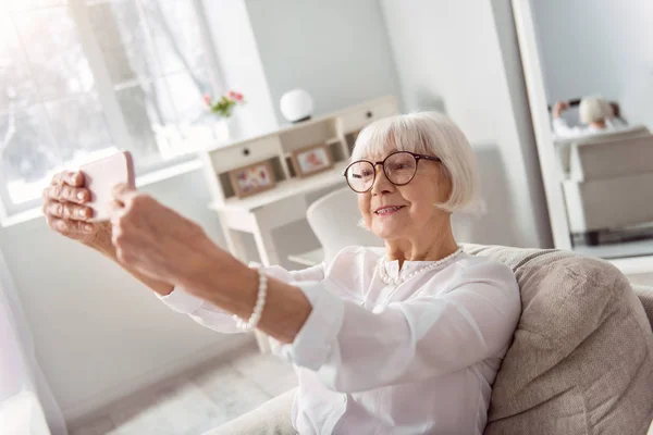 Mulher idosa alegre tomando selfie na sala de estar — Fotografia de Stock