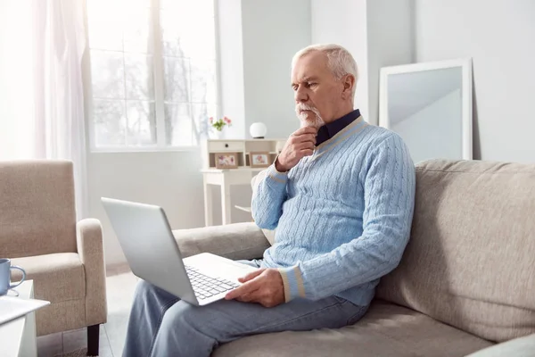 Agradable hombre mayor leyendo desde el ordenador portátil en la sala de estar — Foto de Stock