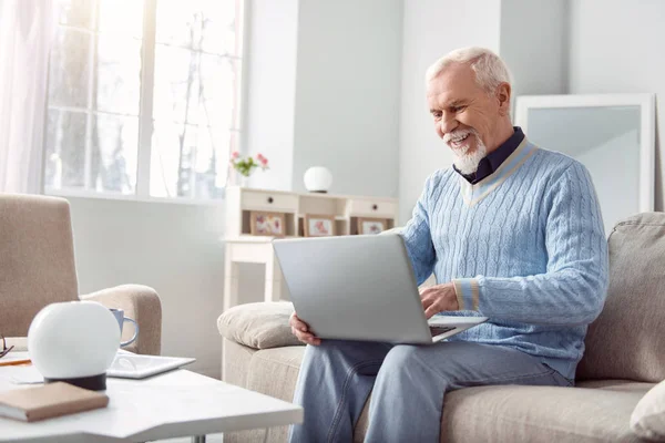 Бодрый пожилой человек использует свой ноутбук в гостиной — стоковое фото