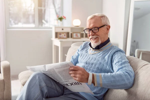 Бодрый пожилой человек улыбается, читая статью в газете — стоковое фото