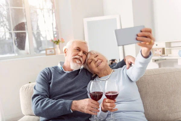 Casal idoso alegre tomando selfie enquanto bebe vinho — Fotografia de Stock