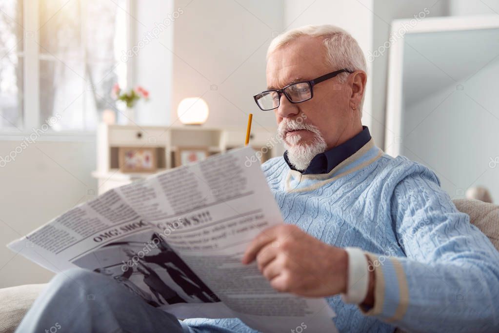 Pleasant senior man reading article in the newspaper