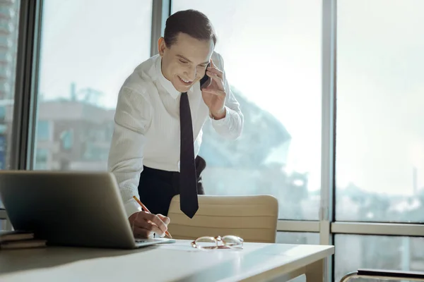 Cheerful executive making notes while talking on phone