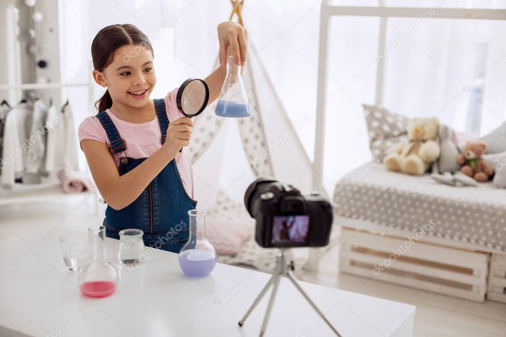 Cute girl examining result of chemical experiment while recording vlog