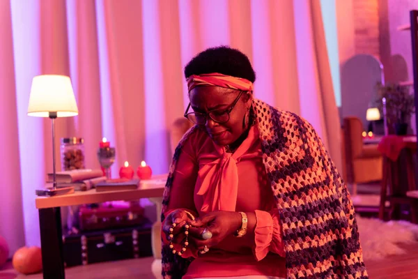 African american plump fortune-teller with big rings looking at the string of beads — Stock Photo, Image