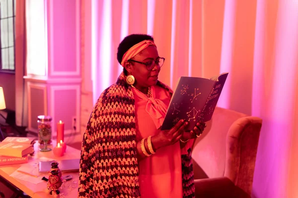 Afro-americano regordeta adivina con grandes anillos sosteniendo un libro sobre adivinación — Foto de Stock