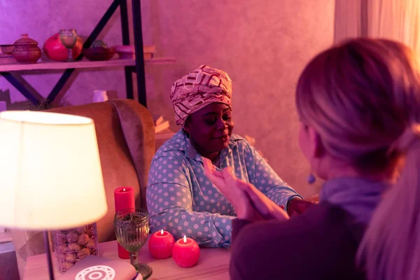 African american plump fortune-teller in ethnic headwear talking to the client — Stock Photo, Image