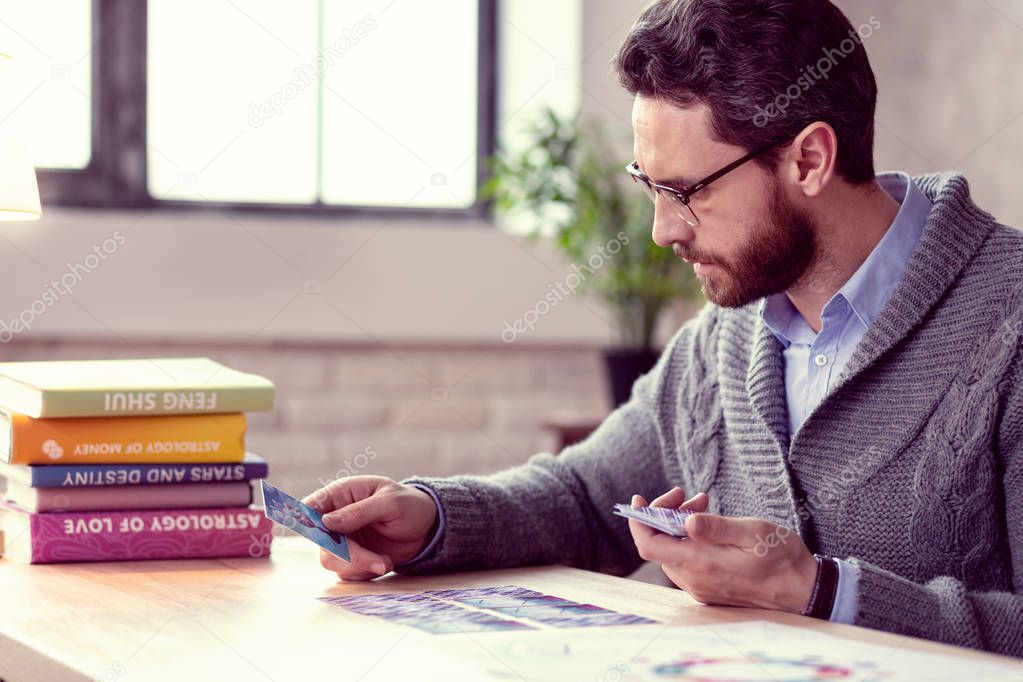 Smart bearded fortune teller looking at tarot cards