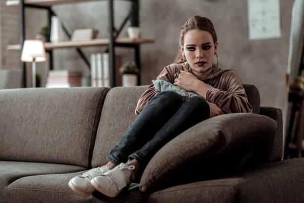 Mörkhårig tonårstjej som sitter på soffan känsla hemskt sprängtryck i gråt — Stockfoto