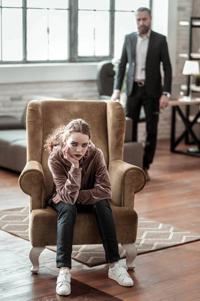 Adolescent bouclé avec un maquillage sombre assis dans un fauteuil confortable — Photo