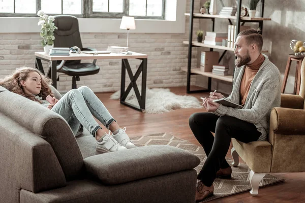 Bearded therapist wearing dark trousers listening to his client — Stock Photo, Image