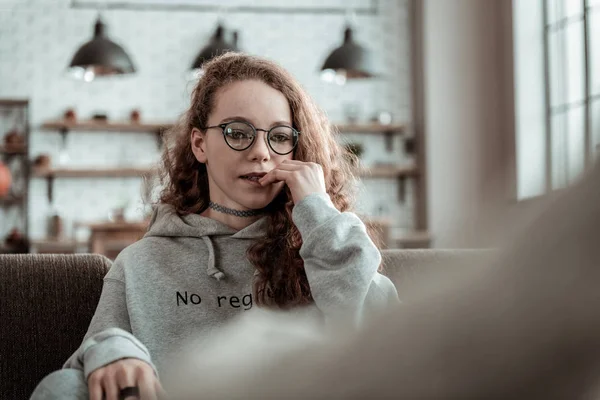 Curly atraente adolescente vestindo capuz cinza sentado no sofá — Fotografia de Stock