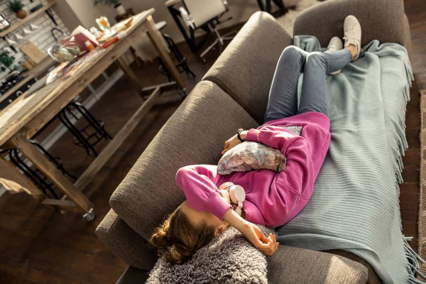 Дівчинка-підліток обіймає маленьку подушку і лежить на дивані вдома — стокове фото
