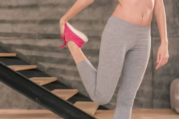 Sottile donna che indossa leggings grigi allungando le gambe dopo il fitness — Foto Stock