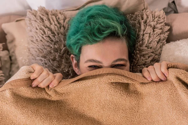 Zelené vlasy žena ležící na měkký hnědý polštář pod plaid — Stock fotografie