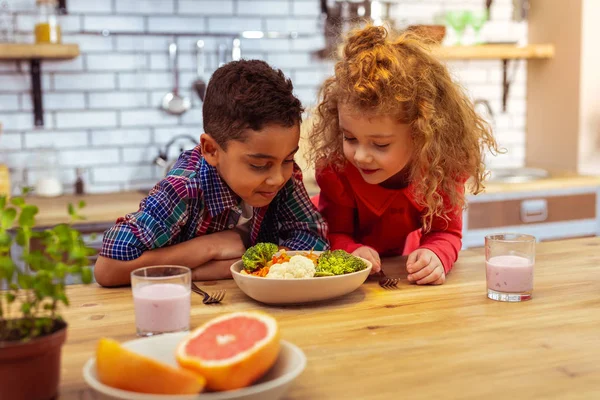 Niños juguetones mirando tazón con verduras —  Fotos de Stock