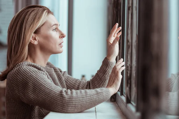 Обеспокоенная женщина, стоящая у окна, чувствует себя подавленной — стоковое фото