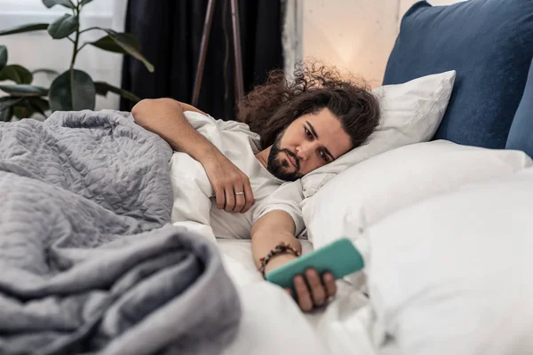 Glädjelös sömnig ung man hålla sin smartphone — Stockfoto