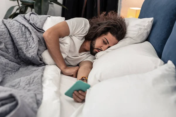 Hombre barbudo soñoliento revisando sus mensajes en la mañana — Foto de Stock