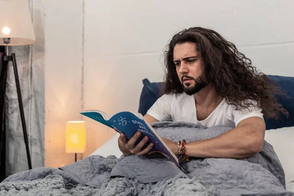 Serious young man reading a book on astrology — Stock Photo, Image