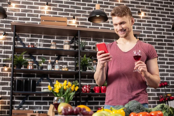 Homem segurando smartphone e copo de vinho esperando namorada em casa — Fotografia de Stock