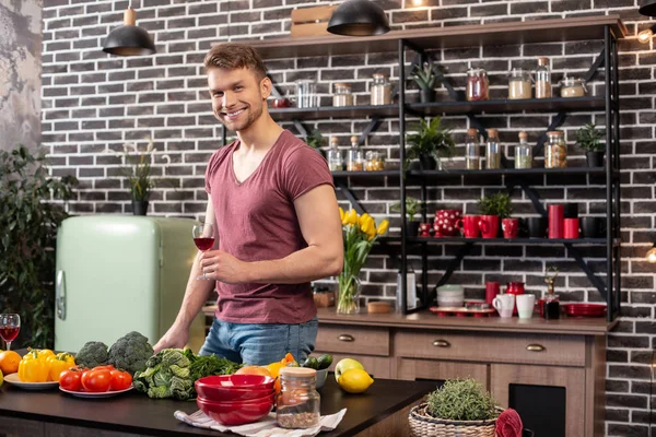 Man with muscles standing in the kitchen and drinking wine