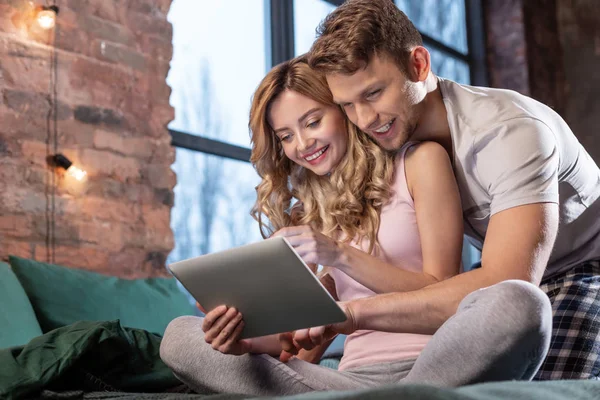 Casal radiante sentado em sua cama confortável e usando tablet — Fotografia de Stock