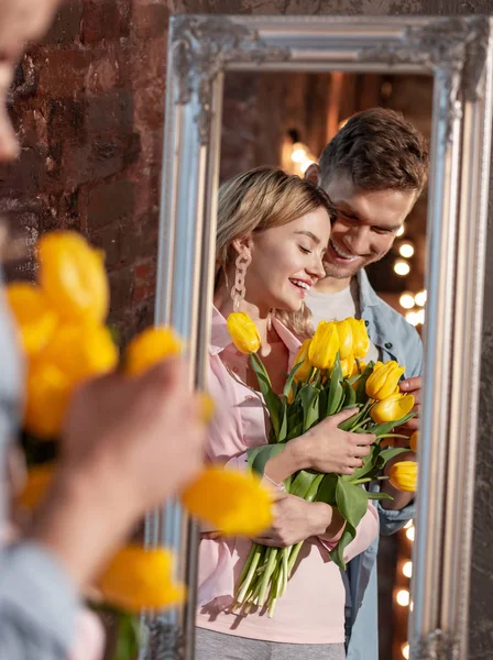 Beaming bela mulher segurando tulipas amarelas de pé perto do marido — Fotografia de Stock