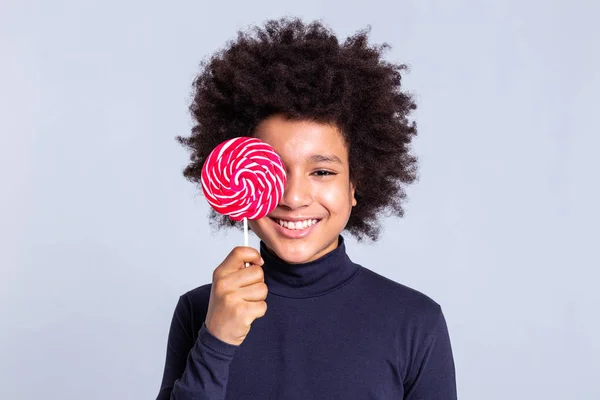 Alegre niño afroamericano con el pelo salvaje cubriendo la cara con grandes dulces — Foto de Stock