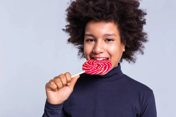 Alegre niño afroamericano mordiendo caramelo rojo pegajoso — Foto de Stock