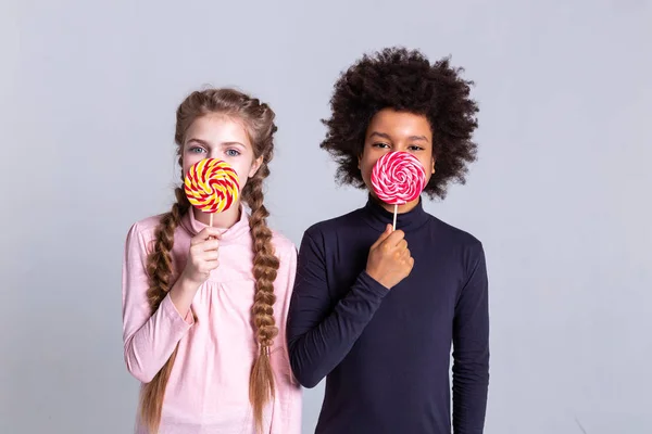 Lindos niños guapos sosteniendo dulces y cubriendo la mitad de la cara —  Fotos de Stock