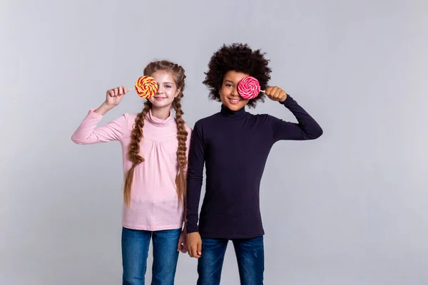 Funky niños pequeños de pie juntos y jugando con caramelos —  Fotos de Stock