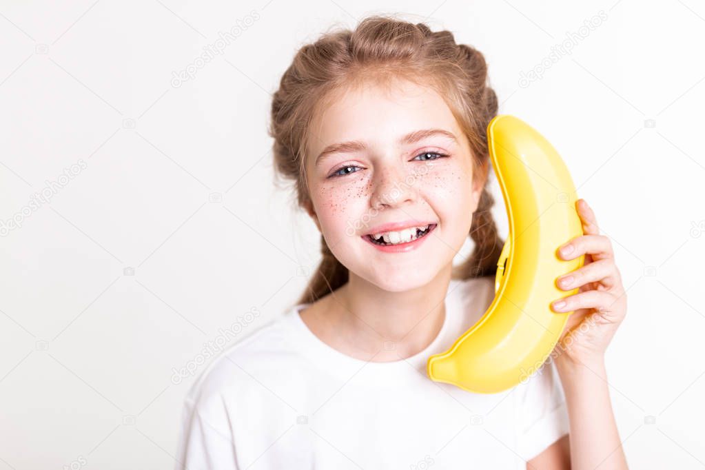 Laughing light-haired young girl holding plastic banana near her ear