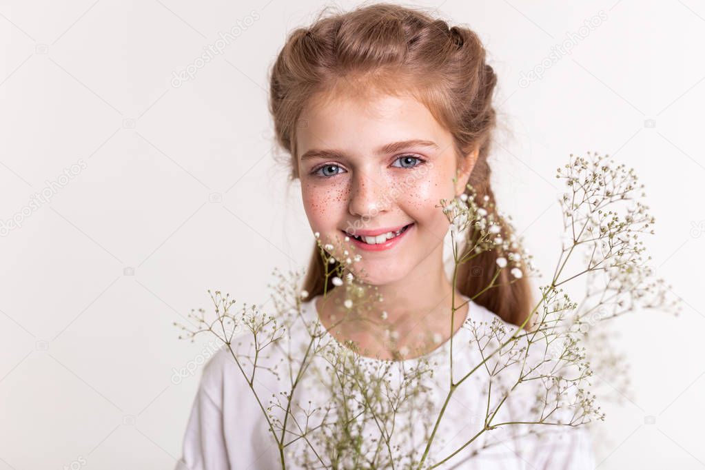 Pleasant good-looking kid looking happy while carrying field flower