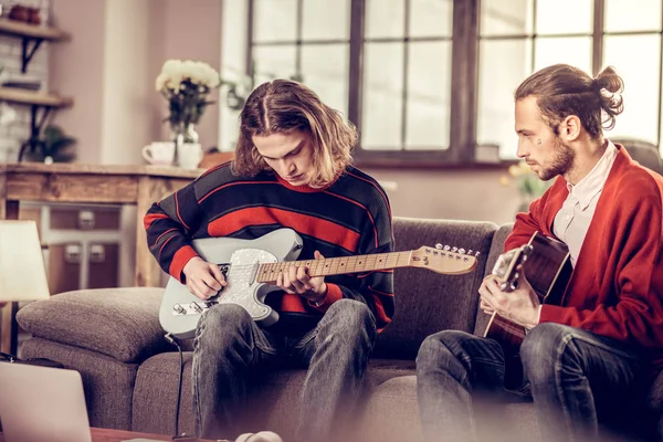 Student with bob cut playing the guitar near his bearded friend