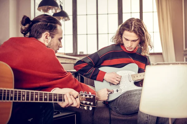 Bearded dark-haired man helping his friend playing the guitar