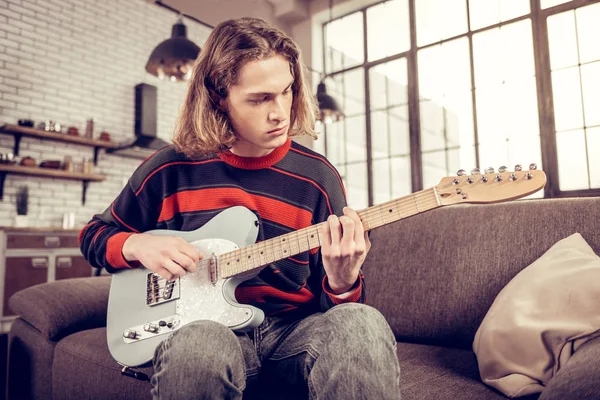 Schöner junger Mann sitzt auf Sofa und komponiert Melodie — Stockfoto