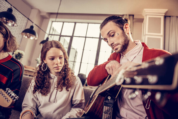 Bearded guitar teacher teaching curly teenage girl at home