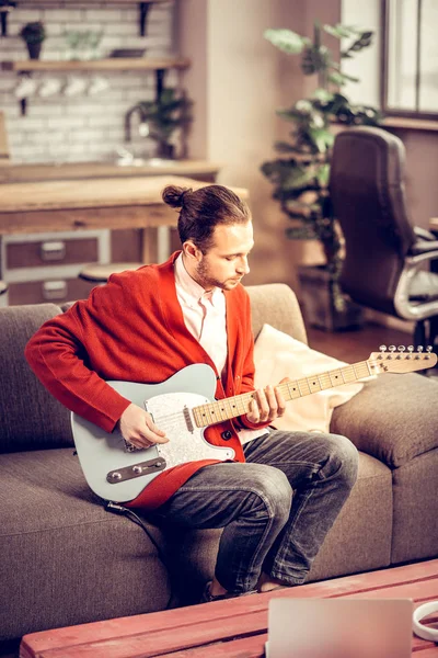 Instrumentalista barbudo sentado en el sofá y tocando la guitarra — Foto de Stock