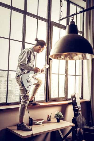 Rockmusiker steht auf Tisch am Fenster und spielt Gitarre — Stockfoto