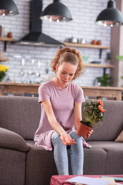 Miserable ginger young lady sitting on grey couch with pot