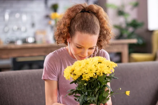 Smiling ginger girl smelling strong scent of flowers — Stock Photo, Image