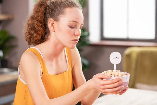 Krullend vrouw bedekt met rode vlekken eenzaam op zoek op etensbak verstoren — Stockfoto