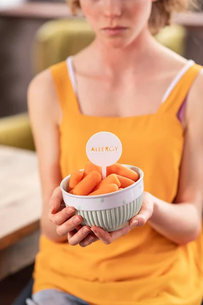 Unhappy skinny girl presenting bowl full of carrots — Stock Photo, Image