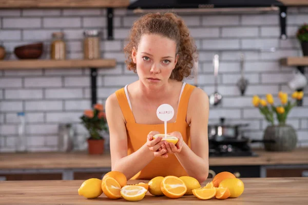Mulher magra inclinada na mesa da cozinha e carregando metade do limão — Fotografia de Stock