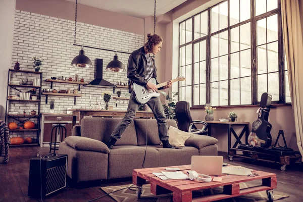 Gek jonge rockmuzikant permanent op sofa en afspelen van muziek — Stockfoto