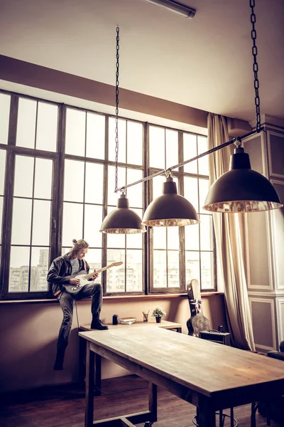 Rock müzisyeni geniş odasında pencere eşiğinde oturuyor — Stok fotoğraf
